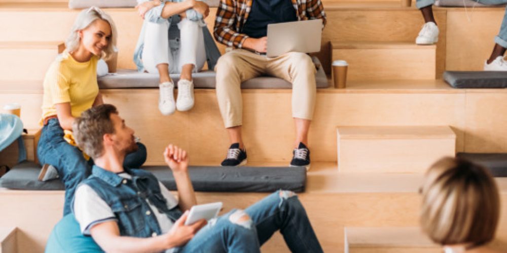 multiethnic young students spending time together at college on wooden tribunes